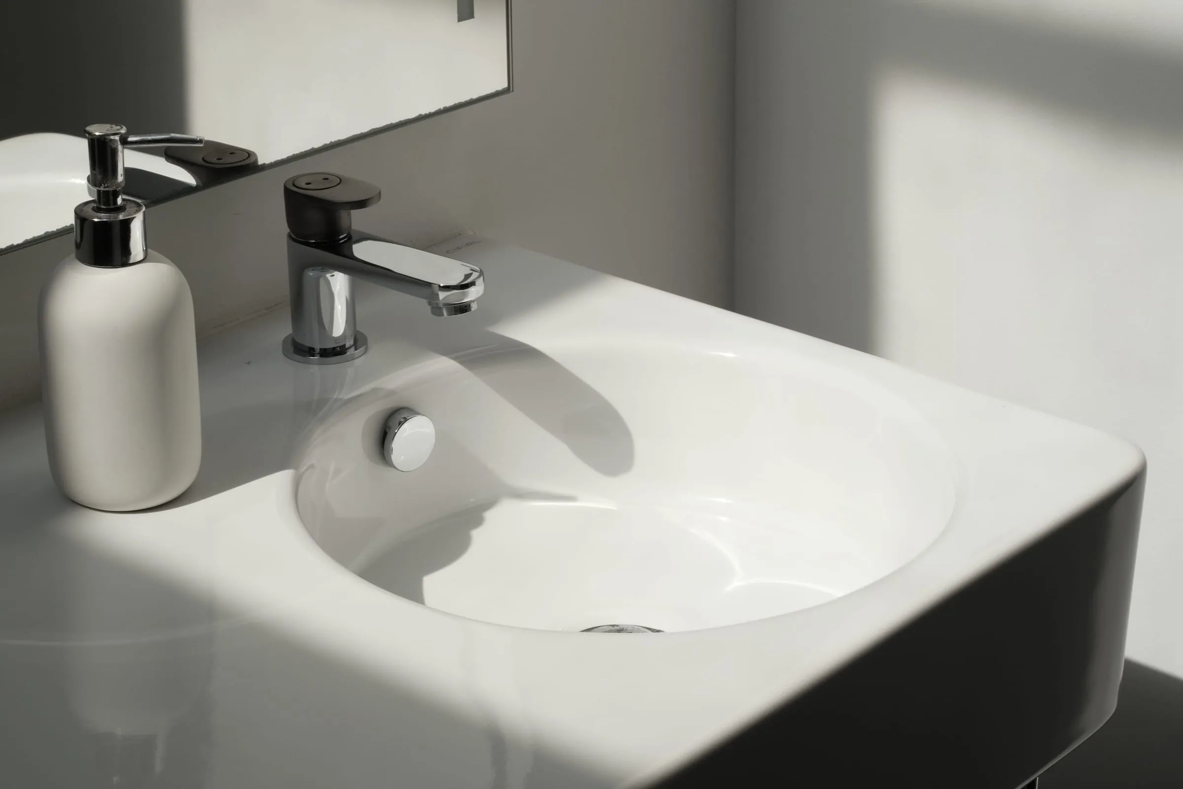 A spotless white bathroom sink and countertop in bright natural light