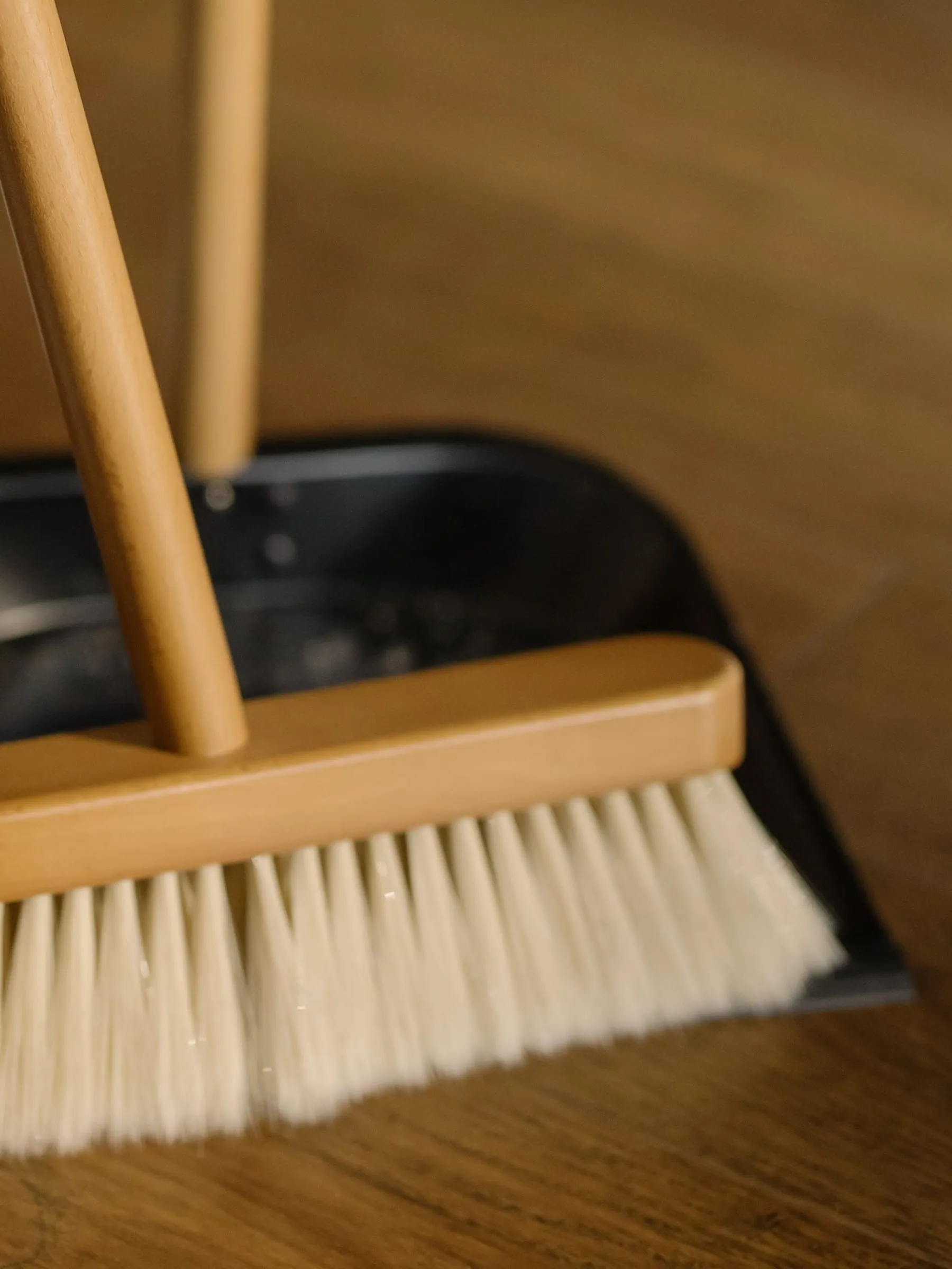 Soft-bristle broom and dustpan resting on a hardwood floor